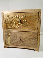 Front view shows the solid wood box with two drawers, detailed brass branch and bird decoration on the top drawer.