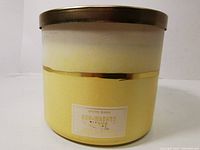 Photo showing cylindrical frosted yellow-to-white candle container with gold band and label.