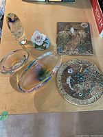 Overview of art glass pieces, porcelain flower sculpture, and ceramic plaques on a wooden surface.