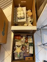 Two boxes containing assorted candles and candle holders including votive, pillar, taper, round candles, tea lights, and sets