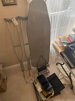 Ironing board, pair of aluminum crutches, black serving tray, and assorted black storage organizers with office supplies on side table