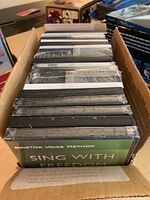 Box containing several instructional DVDs stacked vertically, some shrink-wrapped in original cellophane packaging.