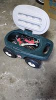 Green plastic Step 2 gardening seat with wheels, hinged lid open showing gardening tools stored inside, including gloves and various metal tools with handles.