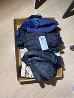 Box with assorted adult winter gloves and hats: black and navy blue quilted gloves, wool hat with multi-color knit pattern.