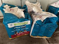 Front view of unopened blue and white Techniseal Smart Sand polymeric sand bags showing branding and usage illustrations.