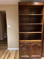 Front view of the wooden bookcase showing four open shelves and double door cabinet with brass pulls and hinges.
