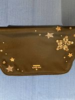 Black Kate Spade small bag with various gold and silver star embellishments on front flap, gold logo plaque at center bottom.