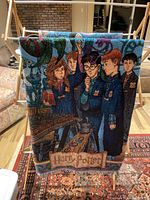 Large Harry Potter woven blanket featuring Hogwarts students and castle, hanging on wooden drying rack