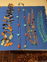 Four Santa Fe style necklaces laid out on blue fabric, showing variety of beads and materials used.