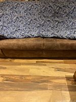 Blue and white paisley patterned comforter laid over a brown leather couch showing pattern and fabric condition.