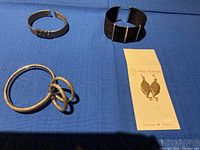 Photo showing two bracelets and three earring items laid out on blue fabric background.