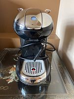 Front view of Illy Francis-Francis espresso maker showing pod insertion area, drip tray with red indicator, power cord wrapped around base.