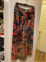 Front view photo of the long floral culottes hung on a black hanger showing the vibrant multicolor floral design on dark fabric.