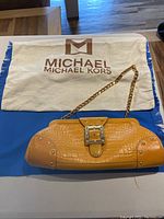 Yellow crocodile embossed leather Michael Kors handbag on a blue surface with branded dust bag in background
