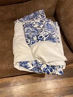 Blue and white patterned dust ruffle folded on a brown couch.