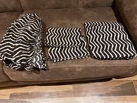 Photo of folded queen size fitted sheet, flat sheet, and two pillowcases with black and white zebra stripes on couch