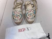 Front view of white leather espadrilles with flower bead embroidery and Red V cloth bag.