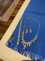 Silver-tone rhinestone necklace, matching drop earrings, and silver rhinestone bracelet laid out on blue fringed fabric.