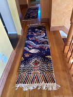 Full length view of the runner rug placed on a wooden floor, showing the dragon design and fringed edge.