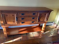 Sideboard closed showing two doors with carved accents and three central drawers with metal handles.