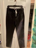 Full view of black faux leather pants hanging on hanger, showing front side and tapered leg design.