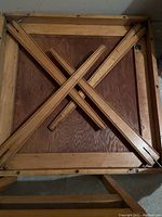 Underside of card table showing wooden folding mechanism with crossed supports.