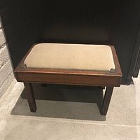 Front view of the antique footstool or bench with beige cotton velvet seat and wooden frame, showing its small size and condition.