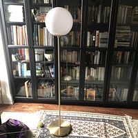 Full view of the tall globe standing lamp positioned near a black glass bookcase, demonstrating overall height and proportion.