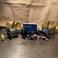 Group photo showing three vintage fishing reels: Penn Peer No. 209, Mitchell 301A with box, and Penn Peerless No. 9, with two yellow reel protective covers.