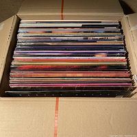 Top view of cardboard box packed with 52 vintage LaserDiscs in cardboard sleeves showing spines and colorful cover edges.