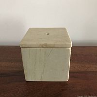 Front view of the square marble travertine box with lid closed showing the pale stone surface and subtle veining.