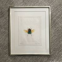 Framed artwork displaying a bee centered with white matting and thin silver frame.