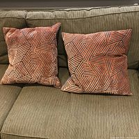 Two standard-size orange throw pillows with black geometric maze pattern laid on beige couch