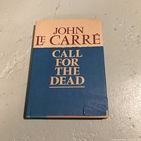 Front cover of the vintage John Le Carré book 'Call for the Dead' showing the dust jacket with visible wear and a tear on the bottom right corner.