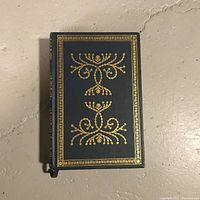 Front cover of vintage hardcover book with gold decorative patterns on dark background.