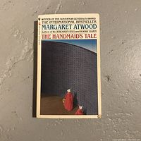 Front cover of The Handmaid's Tale paperback with artwork of two handmaids and a wall, showing author and title text.
