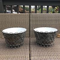 Front-facing photo of pair of vintage metal planters with a rusted exterior and white interiors on brown wicker bench.