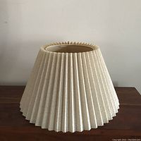 Side view of cream textured pleated lampshade, showing the full shape and design on wooden surface.