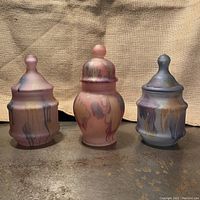 Three vintage hand painted art glass canisters in pastel colors arranged side by side.