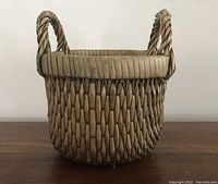 Front view of the vintage woven basket showing the round shape, thick rim, and twisted handles.