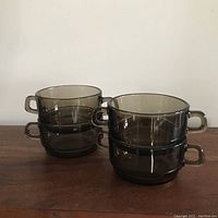 Four stacked vintage smoked glass dishes with handles, showing smoky gray tint and smooth glass finish.