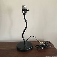 Full view of the vintage squiggle lamp on a surface, showing the curved squiggly stem, circular base, lamp socket, and power cord.