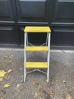 Front view of the step ladder showing the yellow top platform and two yellow steps with gray metal frame.