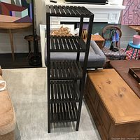 Full view of tall wooden bookshelf utility rack showing four slatted shelves, dark stained wood, situated in a living room environment.