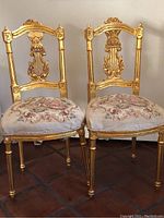 Pair of gold painted antique style replica chairs with floral upholstered seats shown from front view, placed on tiled floor.