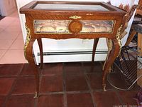 Full view of rectangular wooden antique display table with glass top. Table has curved legs and gold decorative accents.