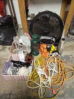 Photo showing the Honeywell floor fan, green camping lantern, two flashlights, assorted extension cords and a puzzle cube, with box containing hardware and twine