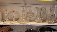 Shelf display of various glass and crystal barware items including decanters, pitchers, candle sticks, and a bowl.