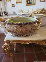 Antique Satsuma hand-painted ceramic bowl with intricate designs and gold detailing shown from front angle on a gold and white table.