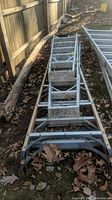Top view of assembled ladders lying on the ground showing dirt, dried leaves and overall wear.